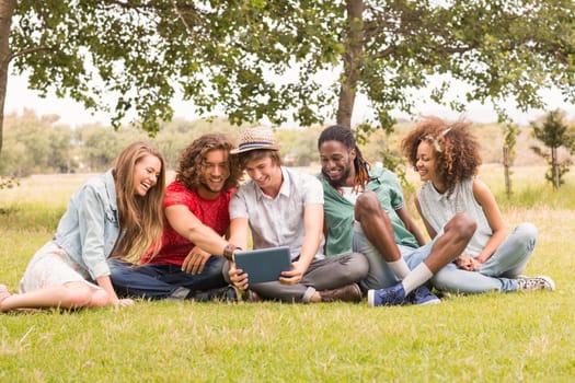 Happy friends in the park looking at tablet on a sunny day