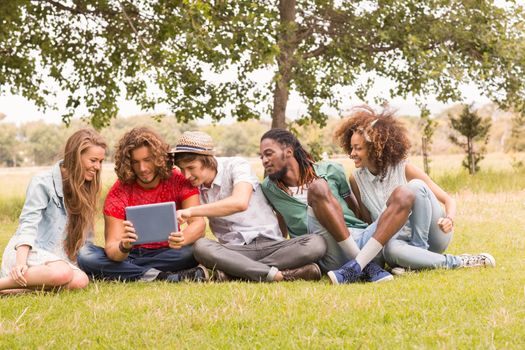 Happy friends in the park looking at tablet on a sunny day