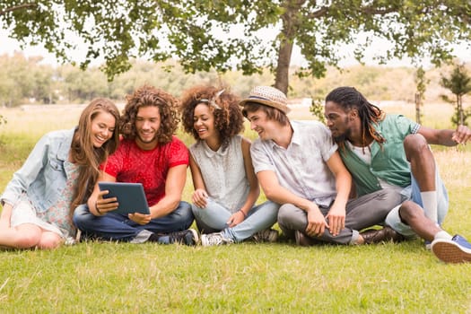 Happy friends in the park looking at tablet on a sunny day