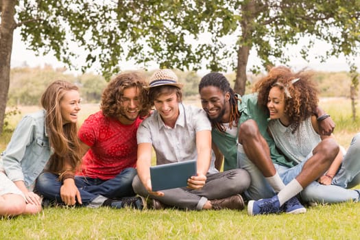 Happy friends in the park looking at tablet on a sunny day