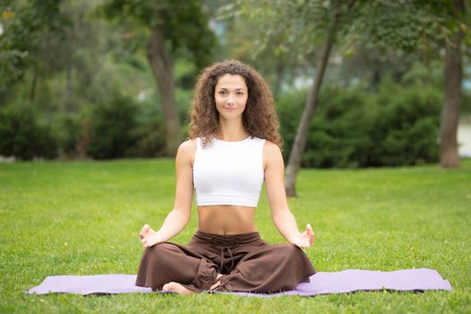 Pretty woman doing yoga exercises in outdoor park, green grass background 