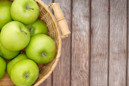 Wicker basket of crisp fresh green apples displayed on a wooden picnic table or at a farmers market for fresh produce direct from the farm, overhead view with copyspace