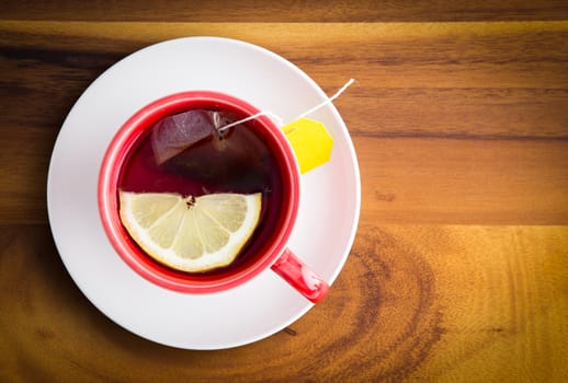 Cup of freshly brewed healthy herbal tea with a lemon slice served in a red cup and white saucer on a wooden table with copyspace, view from above