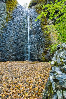 View from the bottom of the Horsetail Falls, Yakima, Washington, USA cascading down a basalt cliff into a small pool below with a foreground of colorful fall leaves