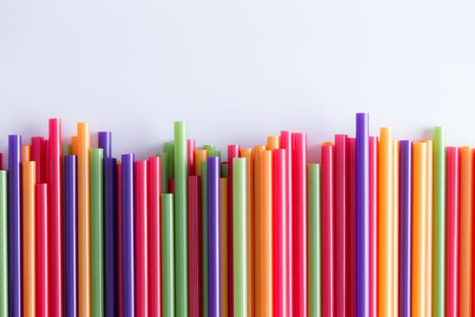 Multicolored vivid plastic drinking straws in a decorative background pattern two-thirds into the frame in an uneven line over a grey background with copyspace for a celebration, holiday or festival