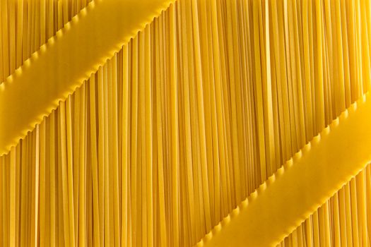 Dried uncooked fettuccini pasta and lasagne background textue with a decorative arrangement of the lasagne as diagonal stripes over the fettuccine, overhead view