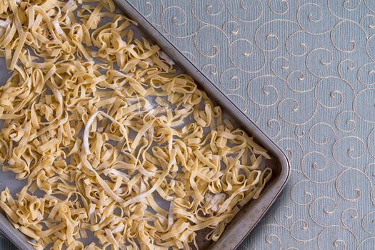Overhead view of fresh homemade fettuccine pasta noodles drying on a metal tray placed on a decorative tablecloth with swirling curlicues and copyspace