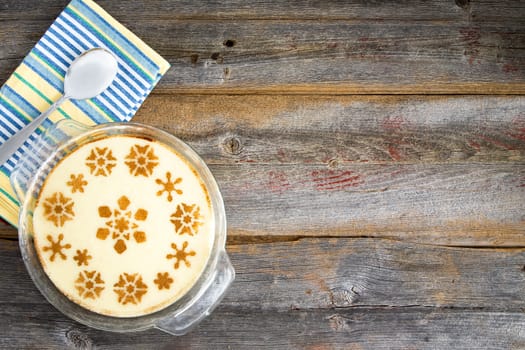 Decorative milky semolina dessert with star or flower patterns on the top in a glass dish viewed from above on a rustic wooden table with copyspace served with a napkin and spoon