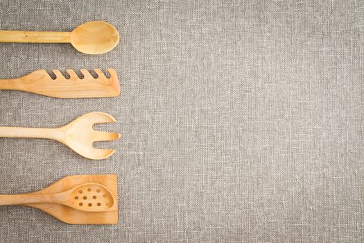 Wooden kitchen utensils for cooks arranged in a line as a side border on a textured beige linen cloth with copyspace and vignette