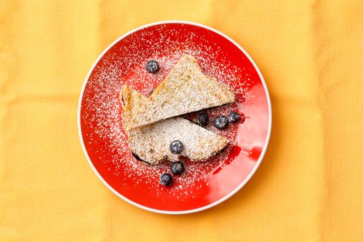 Aerial Shot of a Tasty French Toast Bread with Strawberry Jam Filling on Round Red Plate with Blueberry Fruits. Isolated on Yellow Background.