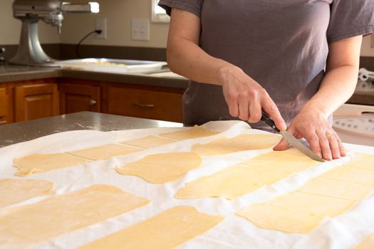 Chef trimming homemade speciality rolled pasta dough in a kitchen cutting it into sheets for making fettuccine so that it can be fed through the pasta cutting machine