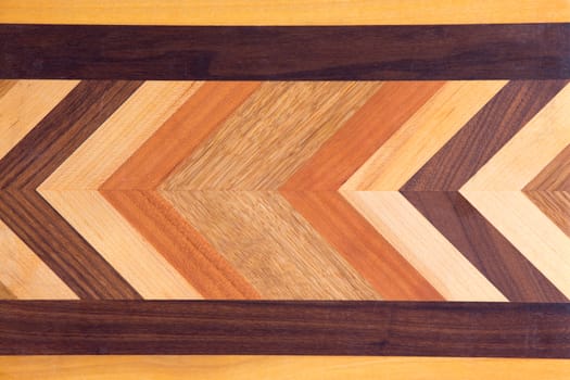 Decorative marquetry on a cutting board with inlaid wood of different colors forming a chevron pattern inside a black linear border, full frame background