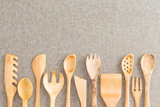 Border of wooden kitchen necessities with the heads of assorted utensils in a row along the bottom of the frame on a beige textile background with copyspace