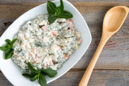 Olivier Salad on old picnic table along with a wooden serving spoon