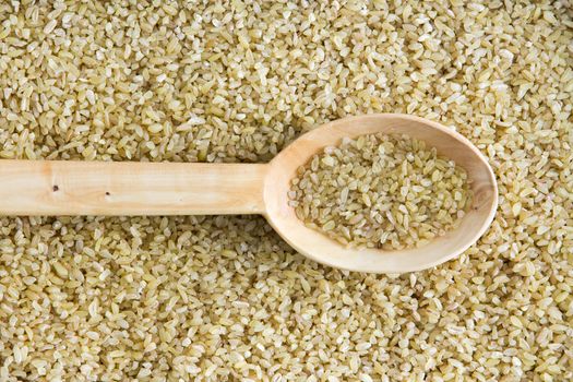 Overhead background texture of dried crushed or cracked wheat with a spoonful in a wooden spoon centered through the frame