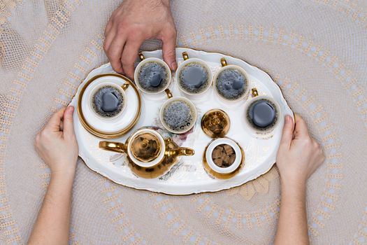 Six Small Cups of Turkish Coffee on a Tray Hold by Hand on Top of a White Table in High Angle View.
