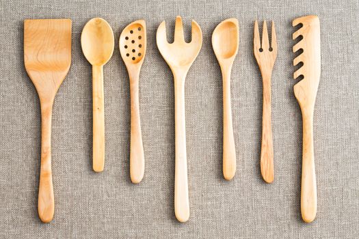 Row of assorted wooden kitchen utensils neatly arranged for size on a neutral beige cloth background viewed from above