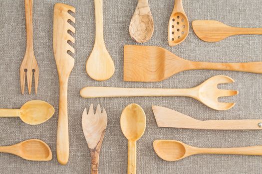 Assorted set of wooden kitchen utensils in an overhead background view with spoons, ladles, pasta drainer, salad servers and draining spoon on a beige tablecloth