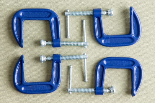 Four blue steel g-clamps neatly arranged on a grey background viewed from above in a DIY, renovation, repair and construction concept