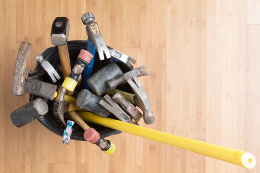 Overhead view of a large selection of different types of hammers for every occasion standing in a bucket on a wooden background with copyspace