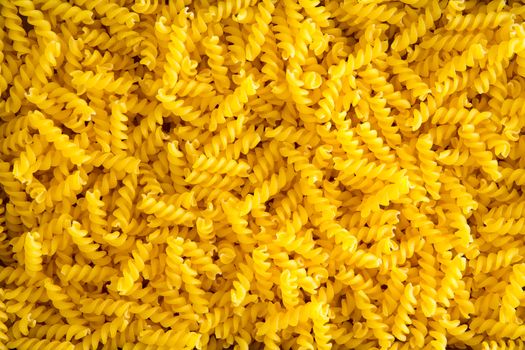 Full frame food background of colorful yellow spiral gluten-free corn and rice fusilli pasta used as an ingredient in Mediterranean cuisine for people with a gluten allergy