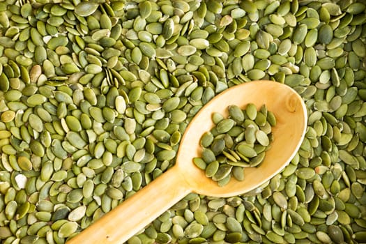 Full frame background texture of fresh cleaned green pumpkin seeds with a rustic wooden spoon arranged diagonally on the surface for use in salads or as a tasty snack