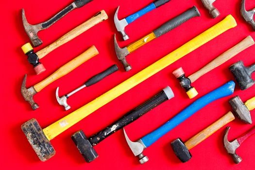 Multiple different mallets and hammers arranged in diagonal lines on a vivid red background in a diversity, DIY, construction, maintenance, and renovation concept, overhead view