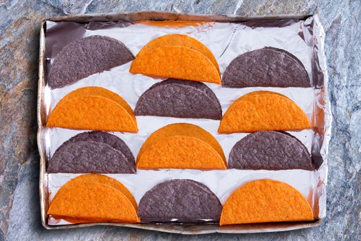 Crunchy tortillas, a traditional flatbread made with cornflour or maize popular in Latin American cuisine, waiting to be heated in the oven arranged in a colorfu alternating pattern in a baking tray