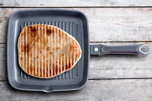 Close up Tasty Grilled Naan Flatbread with Stripe Marks on a Black Square Pan Served on Top of a Wooden Table. Captured in High Angle View.