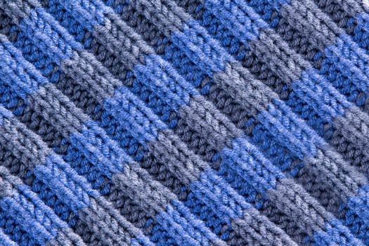 Background texture of handmade crochet work in blue and grey with a wavy repeating ridged pattern with weave, yarn and fiber detail and diagonal ridged lines, full frame close up from above