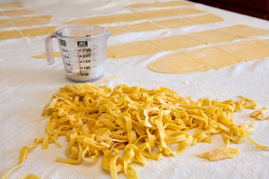 Heap of fresh homemade fettuccine pasta prepared with semolina and durum wheat dough on a kitchen counter with sheets of uncut dough and a measuring jug in the background