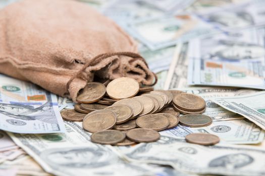 Golden dollar coins spilling from a hessian bag onto a background of US dollar bills with focus to the coins conceptual of wealth, winnings, growth returns, success, graft or money laundering concept