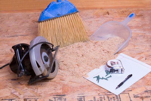 Handheld circular saw with sawdust, brush and pan lying on the floor with a tape measure, pen and nails on a page of paper in a concept of the mess and aftermath of carpentry