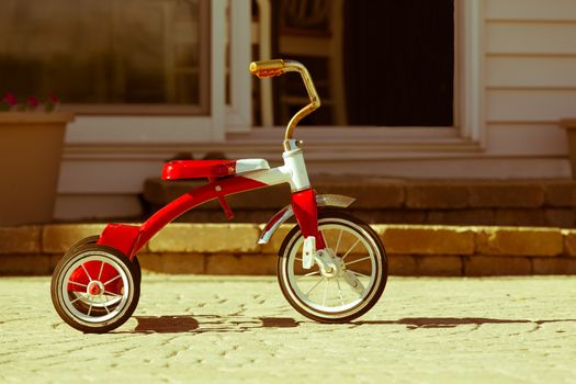 Child's rusted favorite cherished red tricycle standing ready and waiting for its owner to arrive on paving outside a house