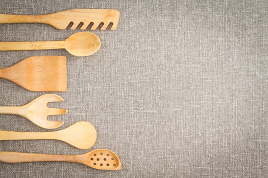 Wooden cooking utensils for food preparation arranged in a curving row as a decorative side border on a neutral beige linen textile with copyspace