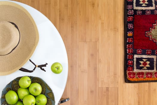 High Angle View of Healthy Fresh Green Apples and Brown Hat on Top of a White Table on the Wooden Floor with Carpet.