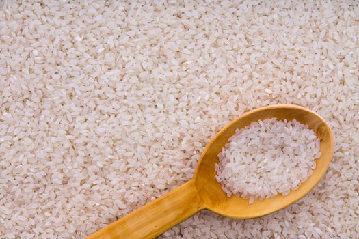 Parboiled rice grains with a rustic wooden kitchen spoon in an overhead background food texture