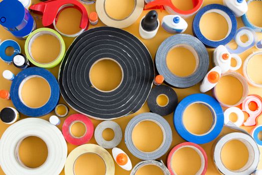 Striking abstract pattern of glue pots and rolls of different types of tape over a yellow background in a random arrangement viewed from above