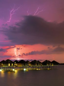 Lightning colouring the sky over water villas at night