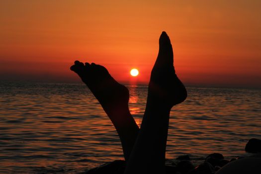 Naked woman legs and evening beach on the sunset