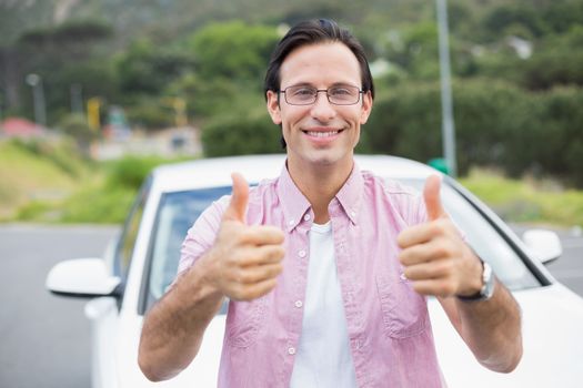 Man smiling at camera showing thumbs up outside his car