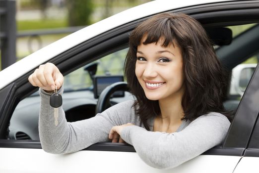 Pretty female driver in a white car showing the car key