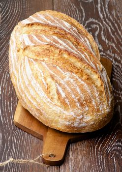 Big Loaf of Homemade Wheat Bread Full Body on Wooden Cutting Board closeup on Dark Wooden background