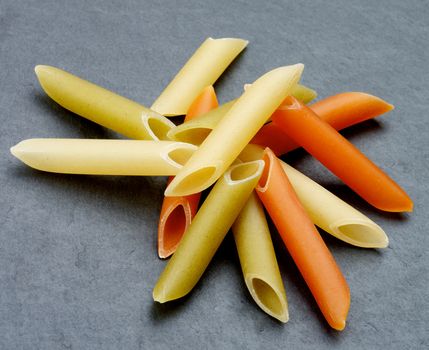 Stack of Raw Penne Triciolore Pasta closeup on Black Stone background