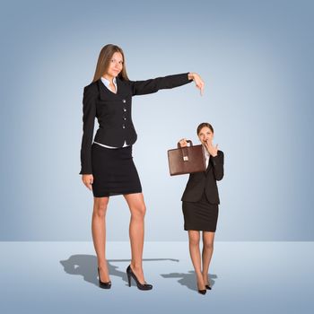 Smiling Young Businesswoman Pointing to small Businesswoman with briefcase. Blue background