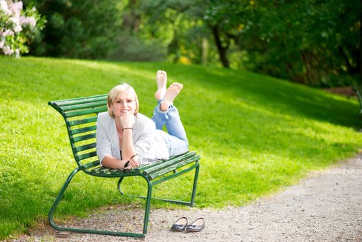 Young woman laying on bench in park and smiling