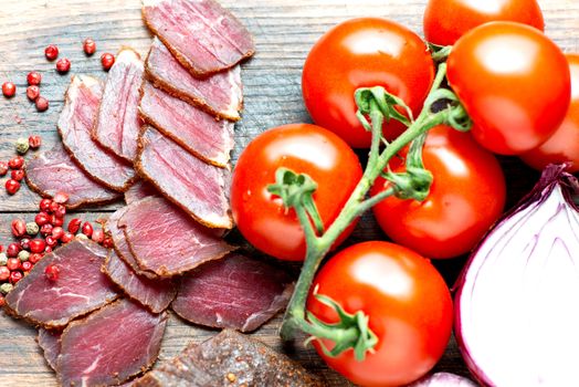 Prosciutto slices, pepper corn and tomatoes on wooden table