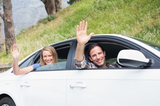 Young couple smiling and waving in their car