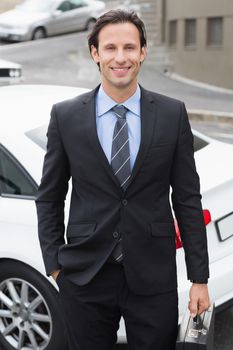 Businessman smiling at the camera outside his car 