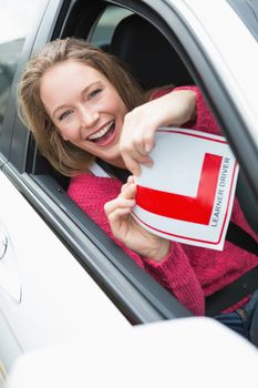 Learner driver smiling and holding l plate in her car
